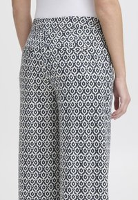 Pantalons larges à motifs présentant un design géométrique bleu marine et blanc, fabriqués dans un tissu doux avec une texture lisse et deux poches arrière.