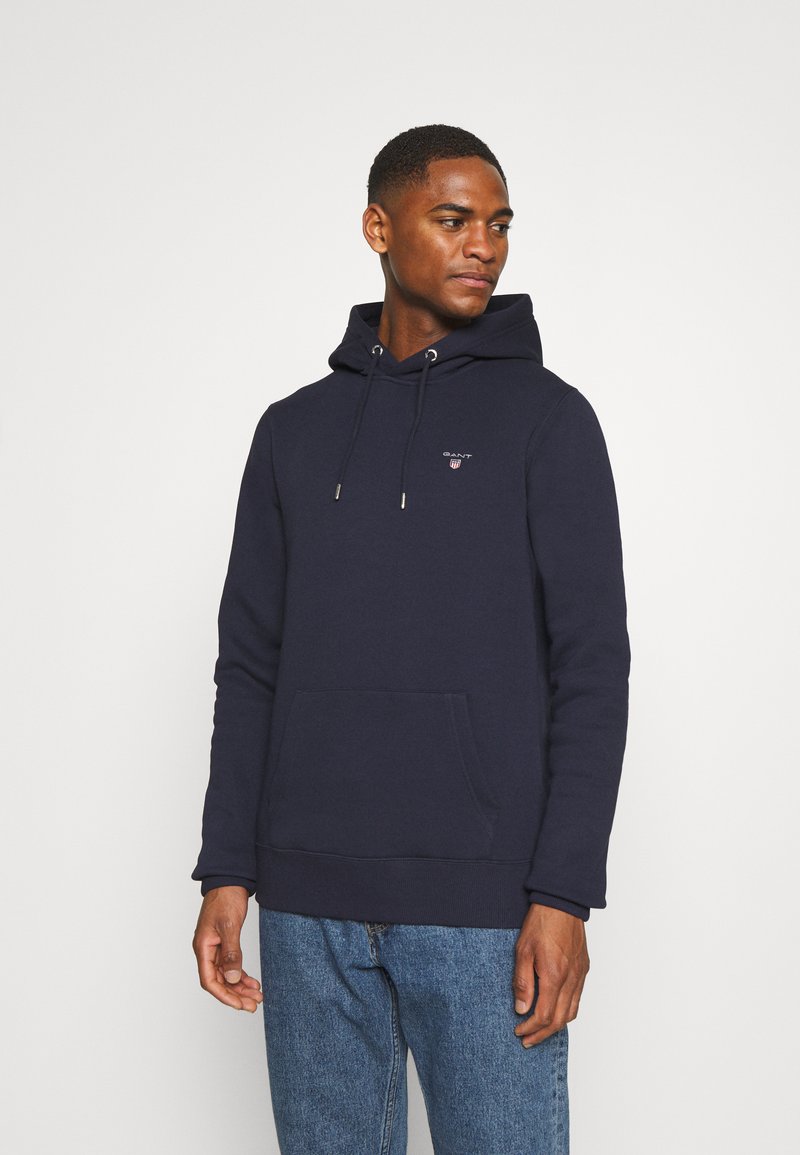 Sudadera con capucha de color azul marino, hecha de tela suave, que cuenta con un bolsillo frontal, cordón y un pequeño logo en el pecho. Ajuste casual.