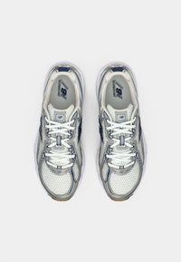 Un par de zapatillas de running New Balance en blanco y gris con acentos en azul marino y cordones blancos, vistas desde arriba sobre un fondo blanco.