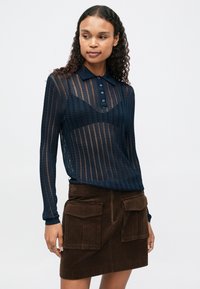 Polo à manches longues tricoté bleu marine avec des rayures verticales et un col, associé à une jupe mini en velours côtelé marron avec des poches avant.