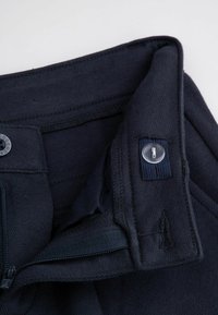 Granatowe spodnie z szerokim paskiem, zapinane na zamek błyskawiczny i guzik, wykonane z teksturowanej tkaniny. Obejmuje małe logo oraz wzmocnione szwy.