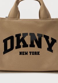 Khaki színű vászontáska fekete fényes "DKNY" logóval és "NEW YORK" felirattal. Két rövid fogantyú, téglalap alakú, texturált felszín.