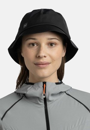 Gorra de cubo negra con un acabado texturizado, que presenta una etiqueta de logo. Combinada con una chaqueta gris claro, destacada por un tirador de cremallera naranja.