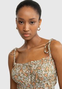 Blumenkleid für den Sommer aus grünem Stoff, mit gerafftem Oberteil und dünnen, verstellbaren Trägern mit gebundenen Akzenten. Kleine, mehrfarbige Blumen sind überall verteilt.