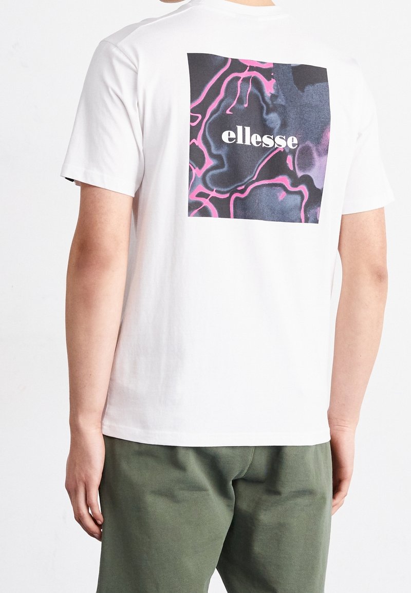 Hvid bomulds t-shirt med et grafisk design på ryggen, der viser sorte og lyserøde abstrakte linjer samt ordet "ellesse" i fed, centreret tekst.