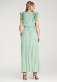 Miętowo-zielona sukienka plisowana z falbaniastymi rękawami, regulowanym paskiem w talii i zwiewnym krojem. Ma długą długość i przezroczysty materiał u dołu.