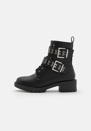 Black ankle boots with a textured finish, featuring two adjustable silver buckle straps and round eyelet details on the sides. Rubber sole.