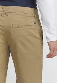 Szorty w kolorze khaki wykonane z bawełnianej tkaniny, charakteryzujące się luźnym krojem, płaskim przodem, dwiema bocznymi kieszeniami, kieszenią z tyłu oraz małym logo.