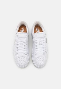 Sneaker bianche in pelle con punta perforata, lacci piatti e dettagli in suede beige. L'interno presenta una soletta in sughero con il marchio Nike Air.