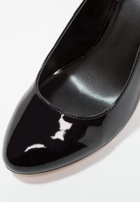 Escarpin femme en cuir verni noir avec bout arrondi et doublure intérieure lisse, montré en gros plan de dessus.