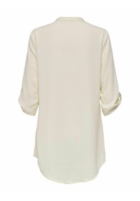 Long-sleeve, light beige blouse with a textured, crinkled fabric. Features a collar and rounded hem, with rolled sleeves.