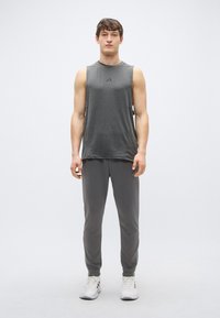 Pelēks bezroku sporta tops ar logotipu, kombinēts ar saskaņotiem pelēkiem sporta biksēm. Modelis valkā baltus sporta apavus. Gluda tekstūra, brīvs piegriezums.