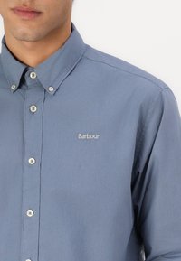 Cămașă albastră deschis, cu guler casual, realizată din bumbac, având cusături decorative și un mic logo brodat "Barbour".
