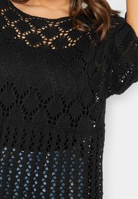 Svart stickad topp med öppen spetsdesign, korta ärmar och en strukturerad design som avslöjar denim under.