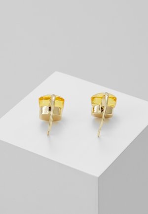 Paire de boucles d'oreilles dorées avec dessus en pierres précieuses jaunes et crochets courbés présentées sur un piédestal blanc.