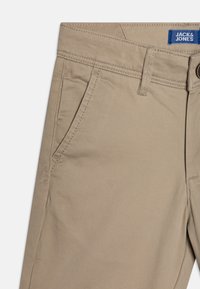 Pantaloni beige a gamba dritta, realizzati in tessuto morbido. Presentano tasche anteriori e una vita cucita con un'etichetta blu.