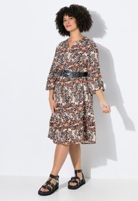 Panterprint jurk in bruin en beige tinten, met driekwart mouwen, een tiered zoom en een zwarte riem. Zwart sandalen maken de outfit af.