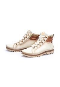 High-top beige leather shoes with brown accents, featuring metal eyelets, textured collar, and a rugged sole for traction. Zipper detail included.