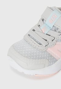 Botte de sport grise avec tige en maille, accents roses et sangle Velcro. Présente une semelle texturée et une zone de renforcement à l'avant.
