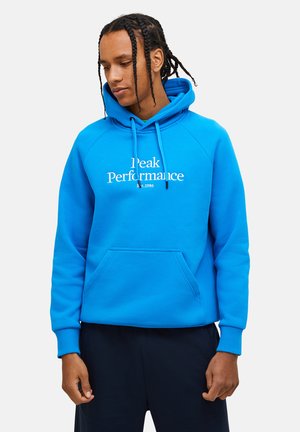 Blauwe hoodie met een kangoeroezak, ribbelmanchetten en "Peak Performance Est. 1986" in het wit gedrukt op de borst. Gladde textuur.