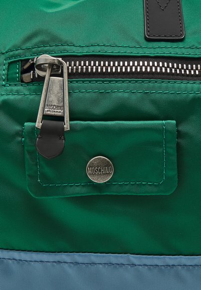 Green nylon bag with a black zip closure and silver hardware. Features a leather accent and a metal Moschino logo on a front pocket.