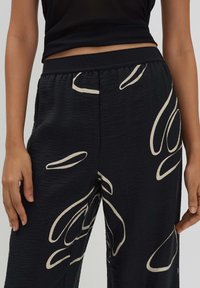 Zwarte broek met een abstract beige patroon, structuurstof, elastische tailleband en zijzakken, gedragen met een aansluitende zwarte top.