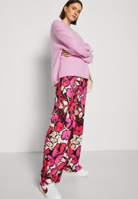 Rosa oversized tröja, blommönstrade vida byxor i svart, rosa och krämfärgat. Vita sneakers med röda detaljer.