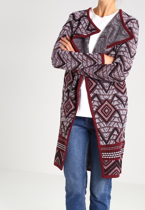 Marinröd mönstrad lång cardigan med geometrisk design, öppen front och texturerat tyg, bärs över en vit topp och blå jeans.