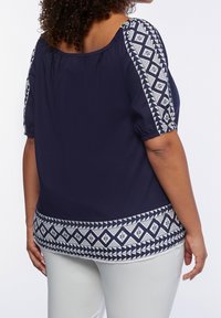 Navy blouse with loose fit, elastic neckline, and short puff sleeves. Contrasting white geometric pattern on sleeves and hem.