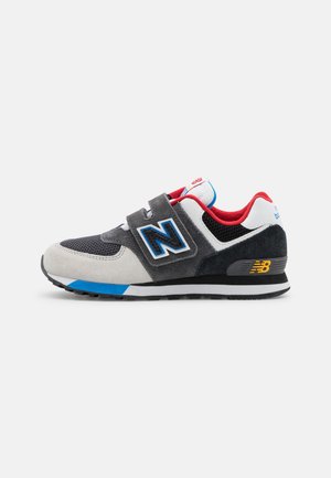 Baskets New Balance gris, noires et blanches avec des accents bleus, une doublure intérieure rouge et deux lanières à Velcro sur un fond blanc.
