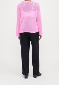 Överdimensionerad rosa stickad tröja med öppen ryggdetalj, kombinerad med svarta byxor. Tröjan har långa ärmar och en lös passform.