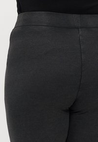 Fekete csíkos leggings, texturált felülettel és elasztikus derékpánttal, hátulról bemutatva, hangsúlyozva illeszkedő kialakításukat.