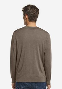Brauner, langärmeliger Pullover aus weichem Material mit rundem Halsausschnitt und gerippten Bündchen, kombiniert mit Jeans.