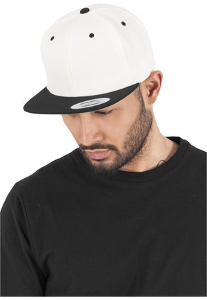 Cappello snapback bianco con visiera nera, caratterizzato da accenti neri sui bottoni in cima, indossato con una t-shirt nera a girocollo.