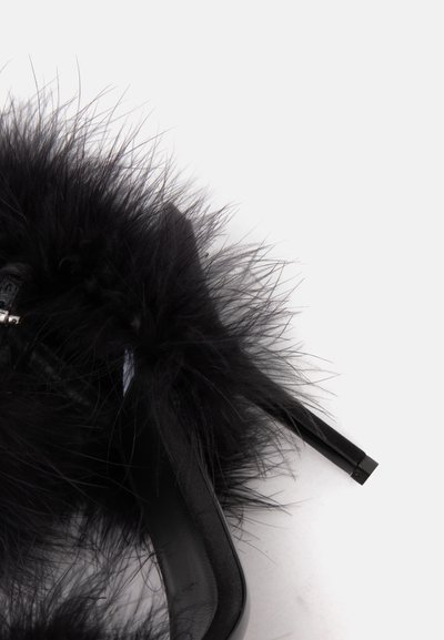 Chaussure à talon haut noire avec un bout pointu et une garniture en plumes noires duveteuses sur fond blanc.