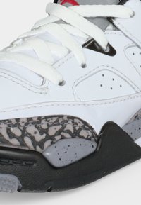 Λευκό αθλητικό παπούτσι με χονδρά λευκά κορδόνια, διάτρητη πλαϊνή επιφάνεια και λεπτομέρεια στη σόλα με μαύρα και γκρι στίγματα.