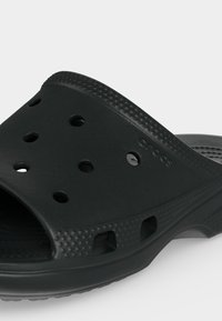 Μαύρο λαστιχένιο παπούτσι τύπου κλογκ με οπές αερισμού, υφασμένο πάτο και το όνομα της μάρκας χαραγμένο στο επάνω μέρος.