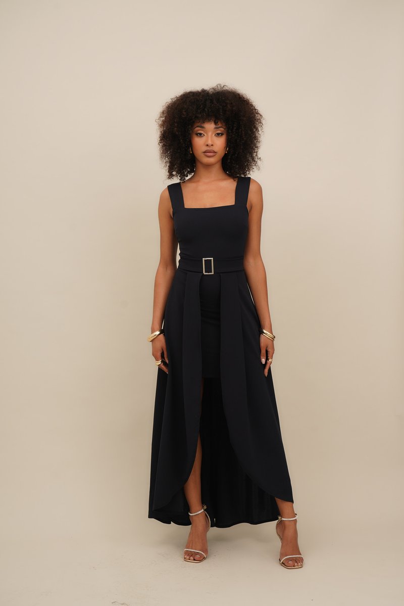 Black dress featuring a square neckline, belted waist, and a flowing skirt with a high slit. Smooth fabric and ankle-strap heels are worn.