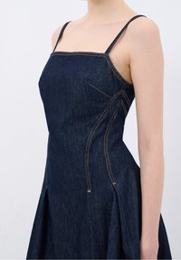 Jeanskleid mit figurbetontem Oberteil, dünnen Trägern und ausgestelltem Rock. Dunkelblauer Stoff mit sichtbaren Nahtdetails und Taschen.