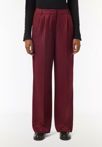 Bordowe spodnie typu wide-leg wykonane z gładkiego materiału, z przodu z plisami i bocznymi kieszeniami. Dopasowane do ciężkich czarnych botków na grubych podeszwach.
