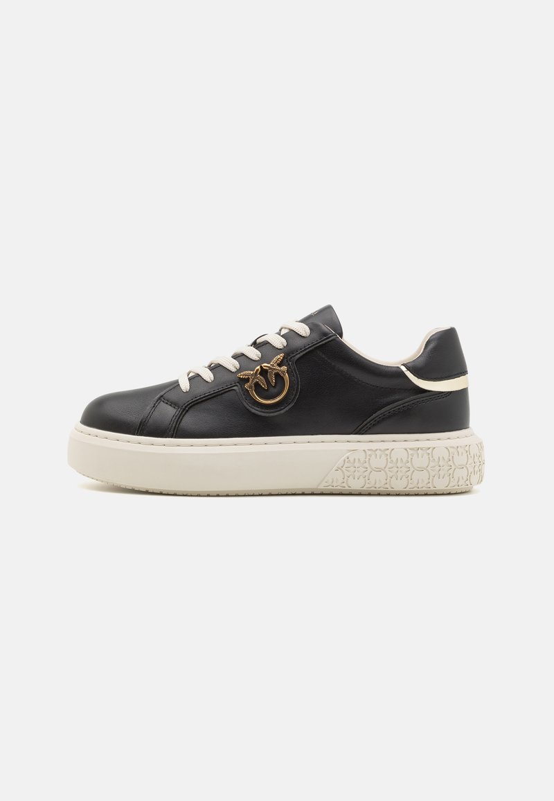 Svarte lær-sneakers med hvit såle, preget av en sirkulær gulldetalj, beige snøring og teksturert detaljering på sålen.