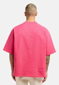 Lyserød oversized t-shirt med korte raglanærmer, lavet af bomuld, med en struktureret overflade og præget logo-detail nær kanten.