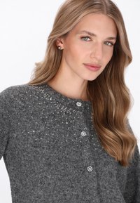 Cardigan tricotat gri, cu guler rotund, dotat cu mărgele decorative, nasturi strălucitori și o textură moale.