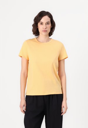 T-shirt en coton jaune à manches courtes, col rond et coupe légèrement ample, associé à un pantalon noir. Texture lisse, sans motifs visibles.