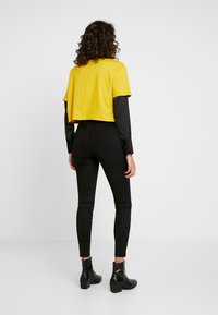 Kortärmad gul t-shirt i kombination med svarta, åtsittande leggings och ankelboots. T-shirten har korta ärmar och en avslappnad design.