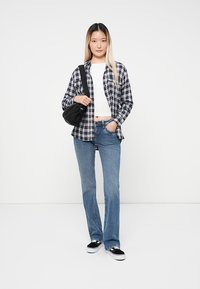 Rutig skjorta i marinblått och vitt, tillsammans med en vit kort topp och ljusblå trumpetjeans. Svart axelväska och svarta sneakers.