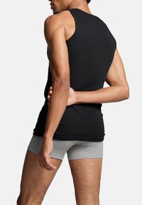 Schwarzes Baumwoll- Tanktop mit enganliegendem Design, das den Rücken und die Schultern zeigt. Ein Paar graue Boxershorts sind ebenfalls sichtbar.