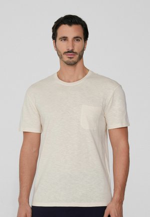 Camiseta de manga corta color crema hecha de tejido ligero, con un bolsillo en el lado izquierdo del pecho y un cuello redondo. Textura suave.