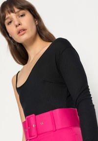 Camisola preta de manga longa com decote profundo, combinada com um cinto largo de um rosa brilhante com uma fivela grande.