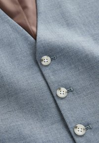 Țesătură de un albastru deschis, cu o textură fină, decorată cu butoane argintii și o căptușeală interioară maro în contrast, având un design de vestă ajustată.